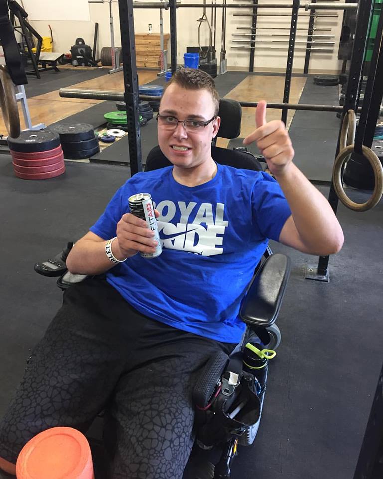 A young man in a weight-lifting gym gives a thumbs-up sign.